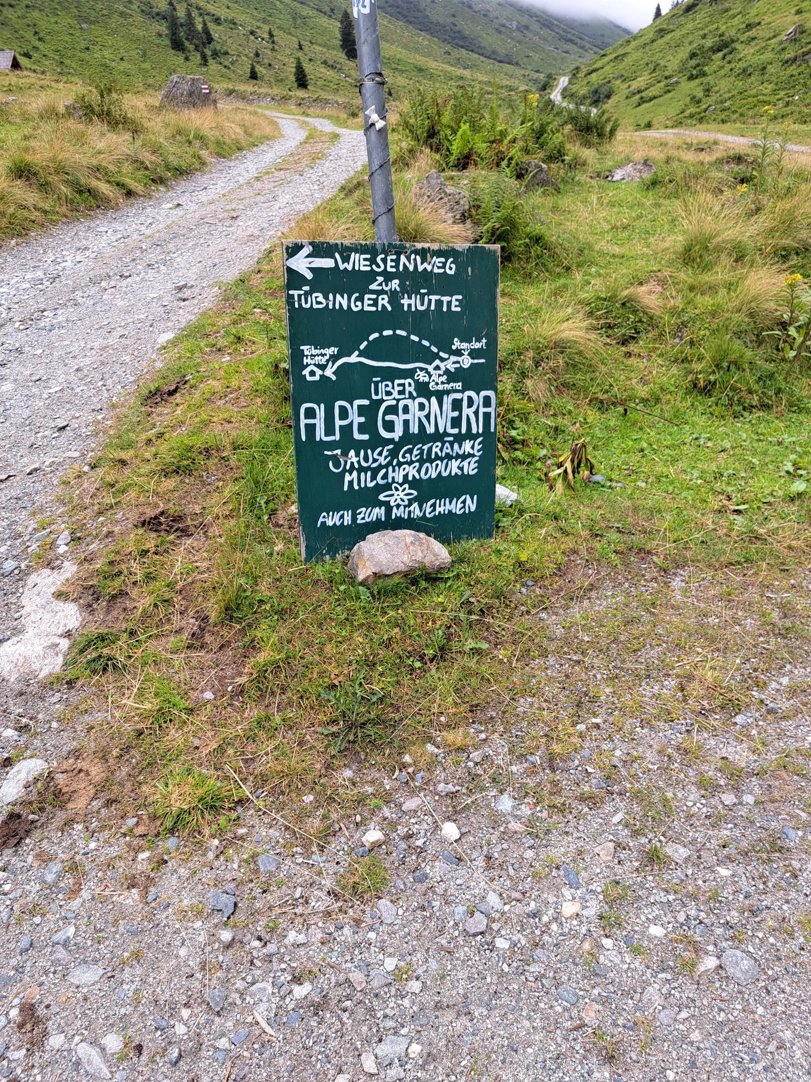 Handgemaltes Wegschild mit der Aufschrift Über Alpe Garnera, Jause, Getränke, Milchprodukte, auch zum Mitnehmen